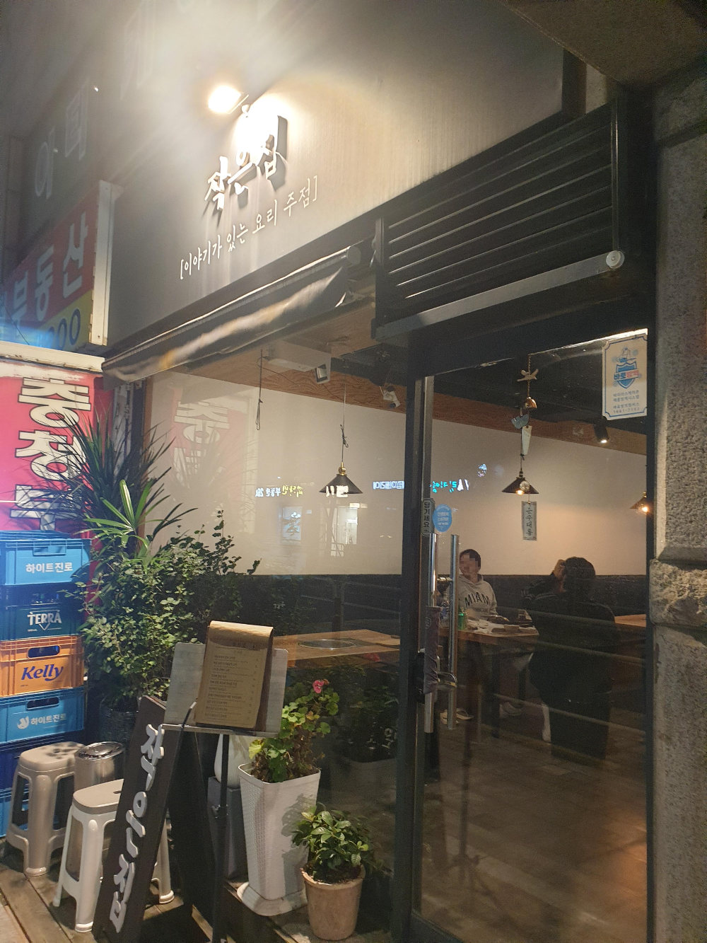 조명이 켜있는 작은집 간판. 유리 안쪽으로 앉아있는 사람 2명이 보인다.