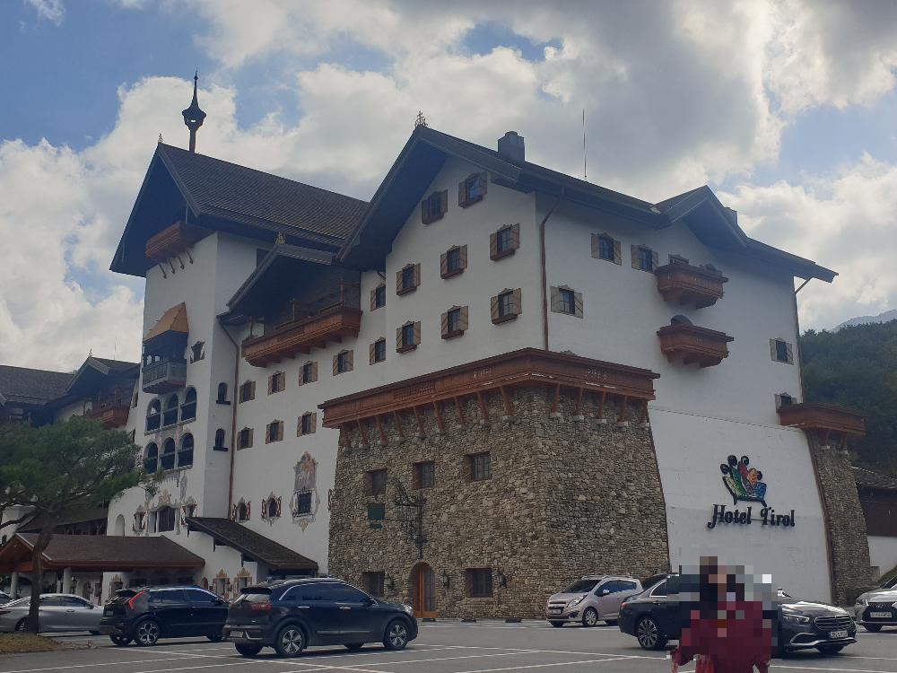 파란 하늘에 구름이 보이고 흰색과 우드 그리고 돌로 만들어진 티롤 호텔