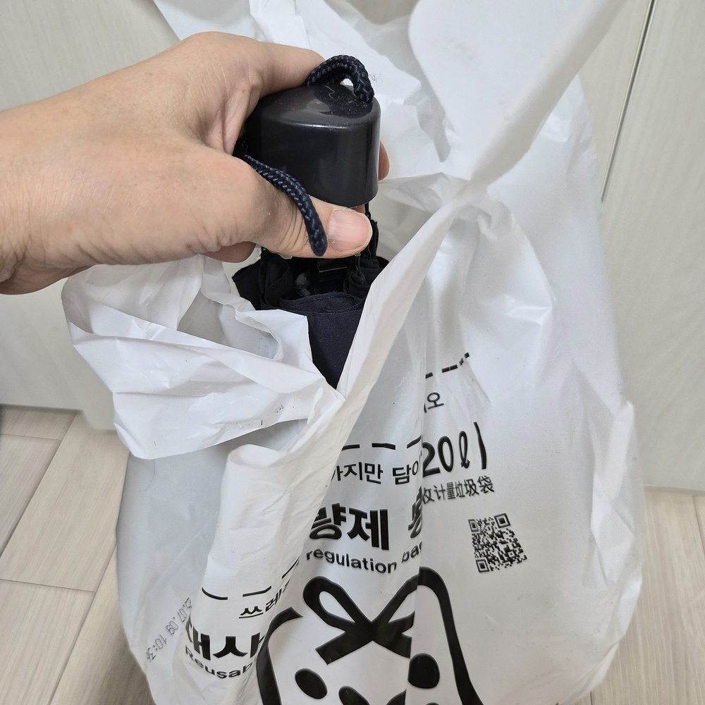 접은 우산을 종량제 봉투에 넣어 일반쓰레기로 정리하는 모습