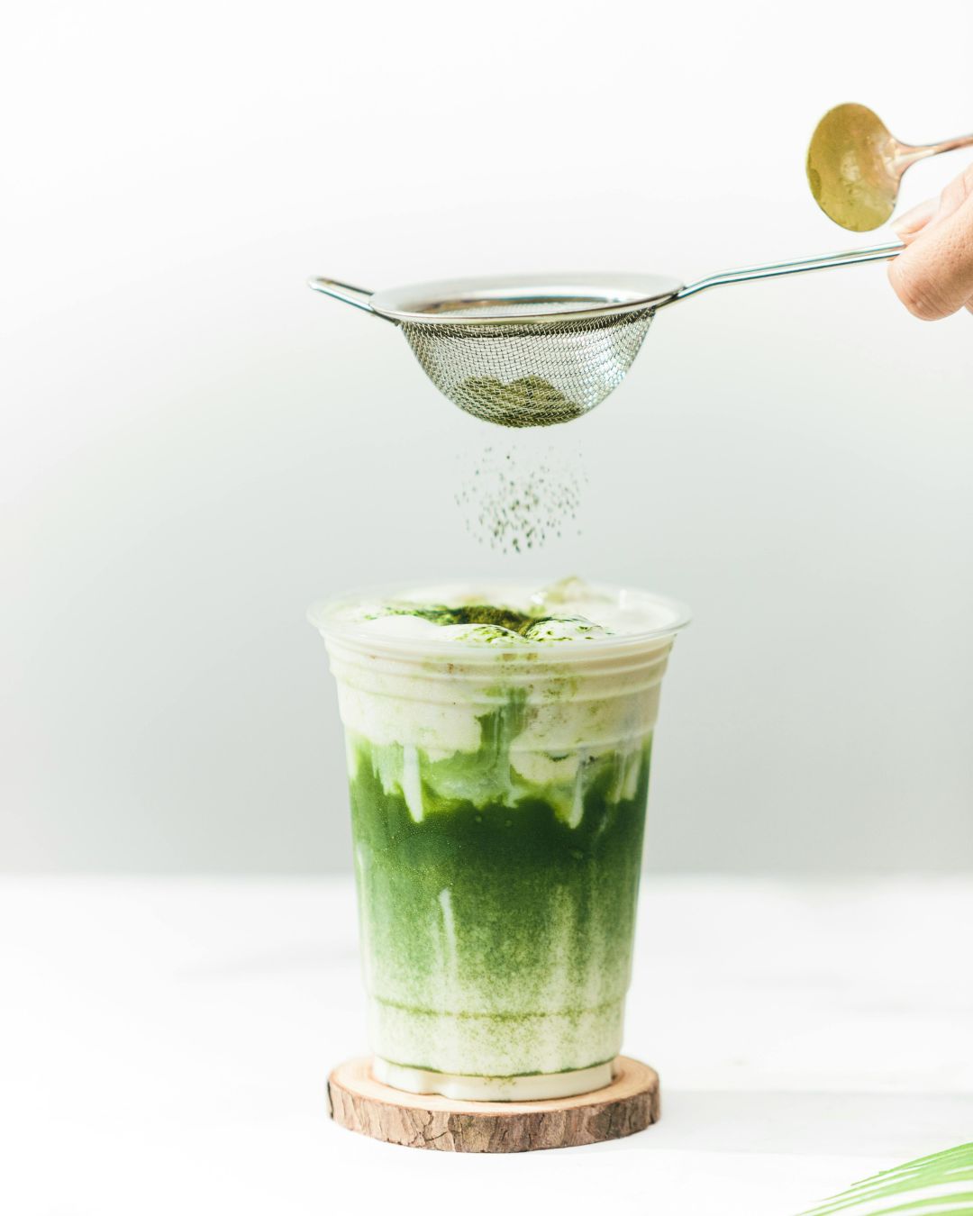 흰 배경 위에 거품 올라간 말차 라떼와 체에 내리는 말차 가루