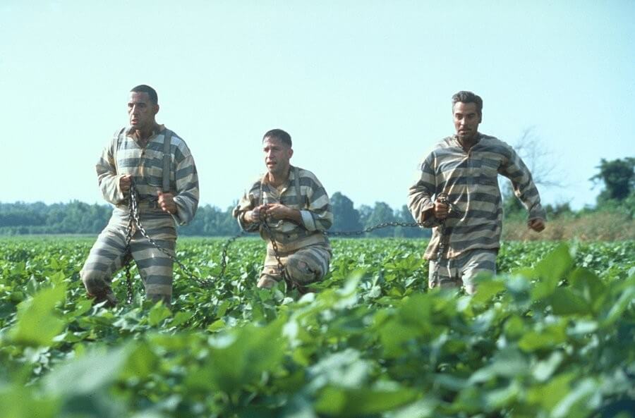 죄수복을 입은 세 남자가 수갑을 찬 채 밭 사이를 뛰어가고 있는 모습