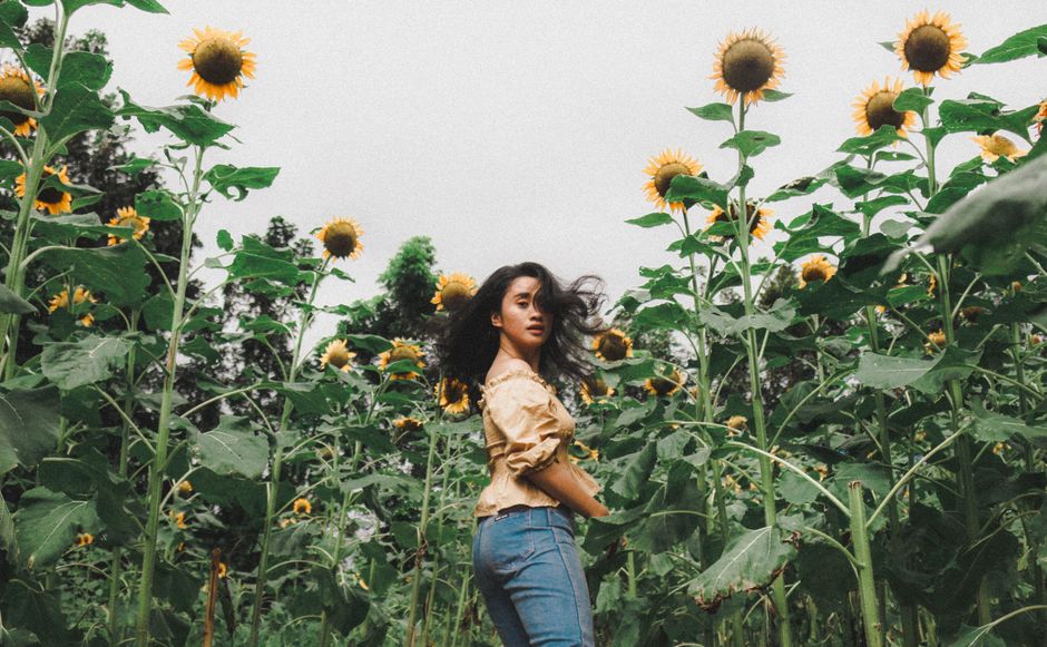 A young woman stands in a vibrant sunflower field, embracing nature.