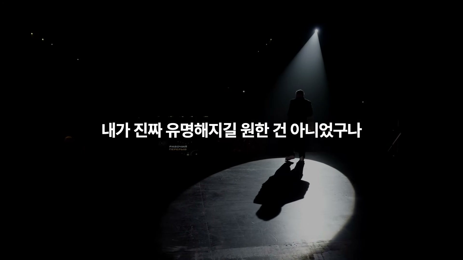 검은 무대 위 둥근 스포트라이트 안에 홀로 선 사람의 실루엣과 자막