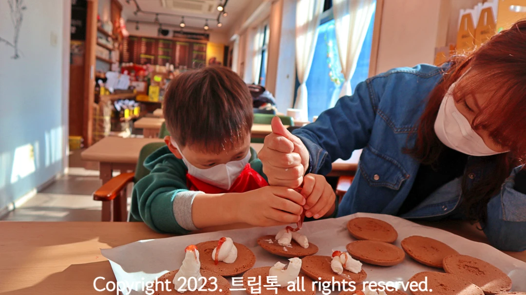 아이가 빵위에 하얀 생크림과 빨간 딸기시럽을 뿌리고 있다.