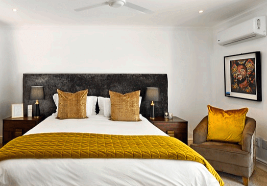 침실에 푹신한 킹사이즈 침대가 있고 오른쪽 벽에는 하얀 벽걸이형 에어컨이 있다.