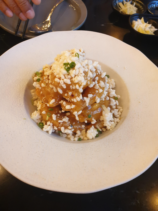 흰접시에 담긴 마라크림새우 위에 누룽지가 뿌려져 있다.