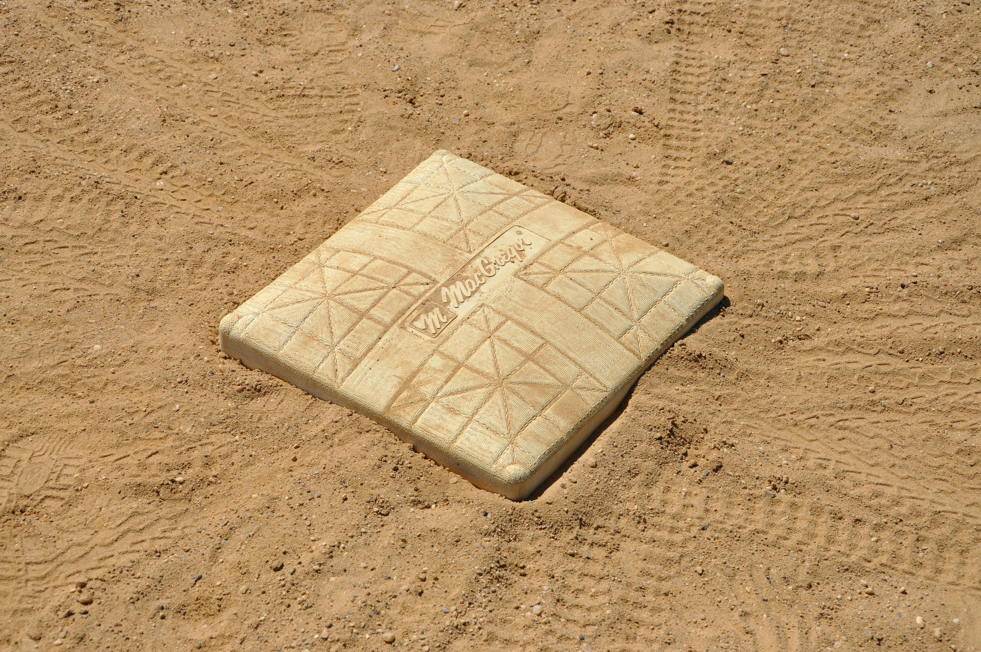 모래와 흙으로 덮인 야구장 위에 놓인 하얀색 베이스 플레이트(루)의 클로즈업 사진.