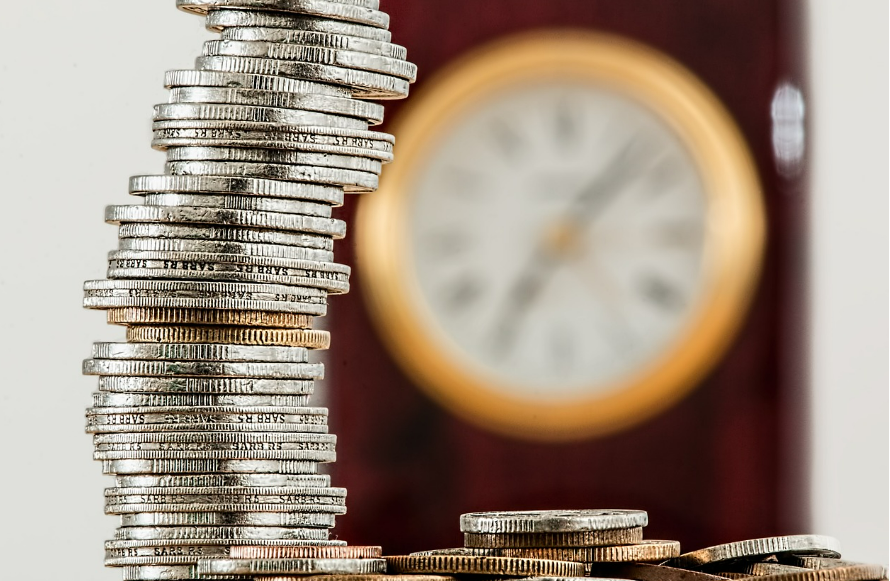 동전이 한 줄로 쌓여 있고 뒤에 흐리게 보이는 시계