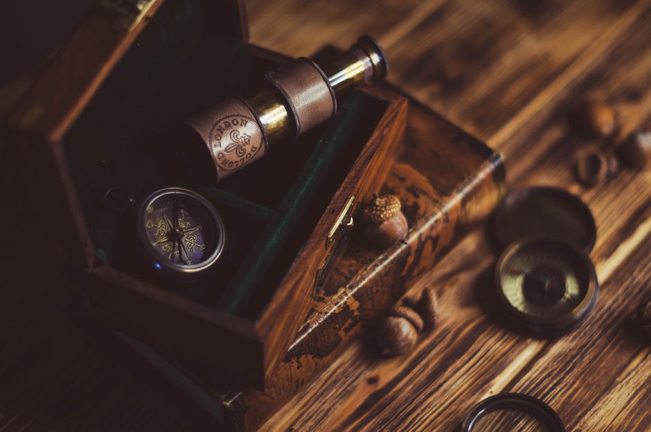 A vintage wooden box containing a telescope and compass on a rustic table.