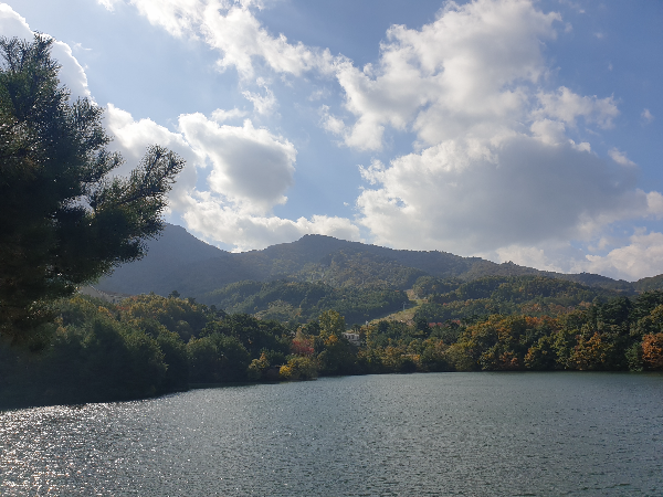 파란하늘과 구름 아래에는 호수가 보인다. 나무들이 조금씩 노랗게 물들어가고 있다.