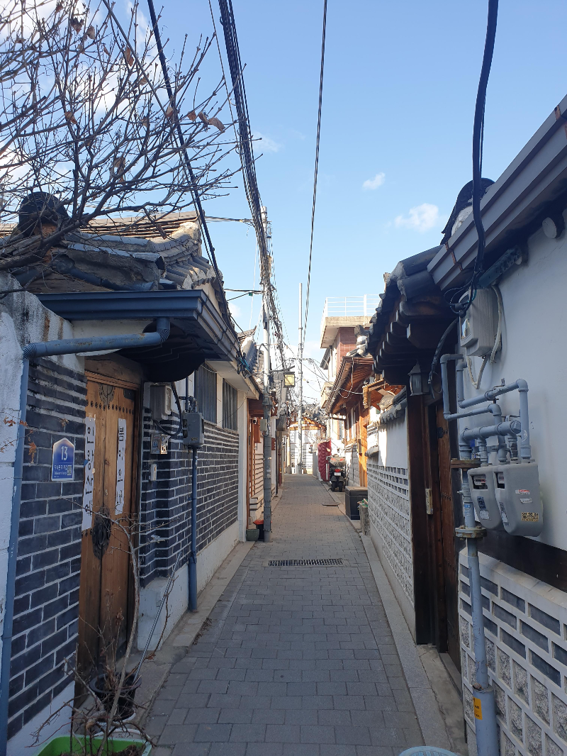 파란 사늘 아래 한옥이 줄지어 있는 한옥 골목. 전선이 밖에 나와 나름의 감성을 만들어낸다.