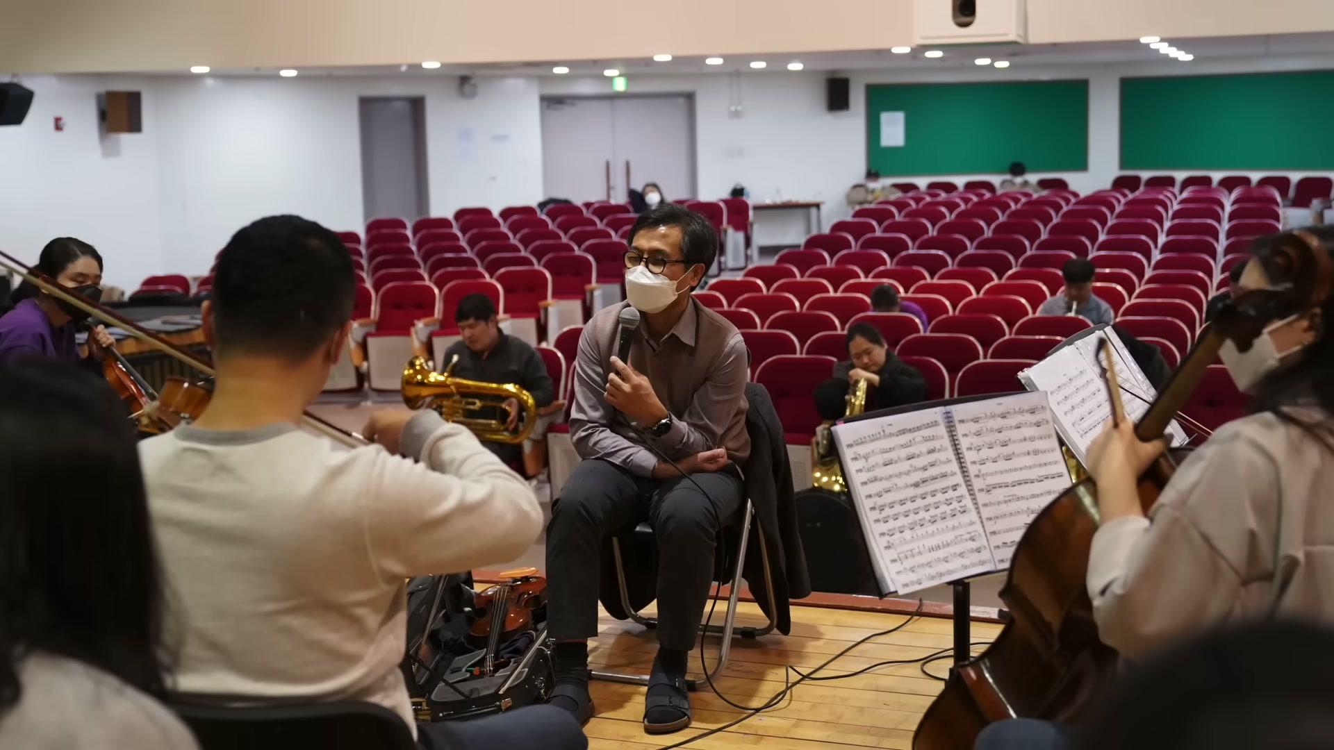 공연장 좌석을 등진 채 마이크를 들고 앉은 김종훈을 둘러싸고 첼로&middot;바이올린&middot;튜바를 든 단원들이 리허설을 하고 있는 모습