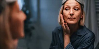 거울로 얼굴에 주름을 보고있는 중년여성 사진