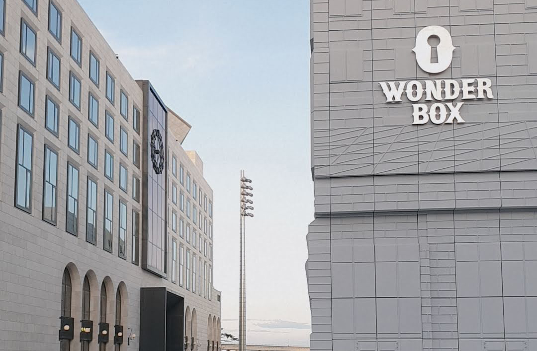 파라다이스시티 원더박스 외관 전경. 회색 건물에 열쇠 구멍 모양의 로고와 'WONDER BOX' 글자가 선명하게 보이며, 주변에 호텔 건물과 조명이 함께 배치되어 있다.