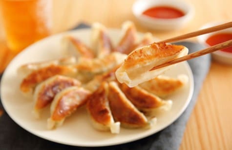 만두가 하얀 접시위에 있고 젓가락으로 만두는 집고 있는 사진