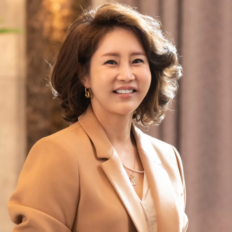 어느 실내를 배경으로 갈색 웨이브 머리에 베이지색 정장을 입고 화려한 악세사리로 치장하고 서 있는 드라마 7인의 탈출의 차주란 캐릭터