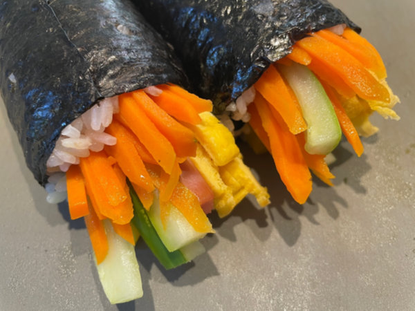 Brushing sesame oil on Rumi Kimbap roll, sprinkling roasted sesame seeds on kimbap