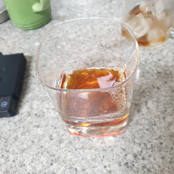 컵에 커피가 담겨있다. 주변에는 초록색컵, 저울, 그리고 서버의 일부가 보인다.