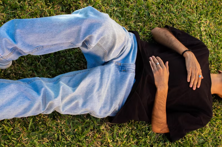 잔디밭에 누워 복부에 손을 올리고 있는 사람의 모습, 위염이나 속쓰림으로 인한 불편함을 표현한 장면