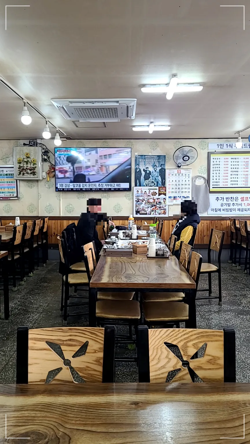 식당 내부의 나무테이블과 나무의자들 테이블에서 식사를 하는 노부부, 벽면에 tv 벽면에 메뉴판이 붙어있음