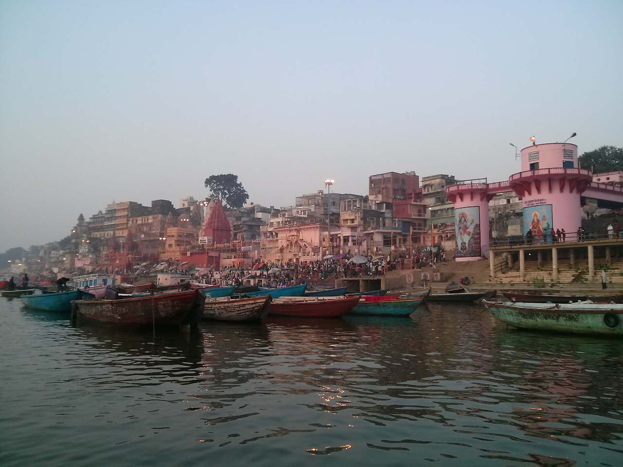 분홍색 원통형 건물에 힌두교 신들의 벽화가 크게 그려져 있고, 계단에서 사람들이 목욕하거나 모여 있는 풍경