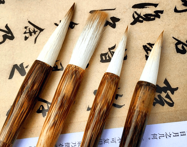 한문이 적힌 종이 위에 붓 4개가 가지런히 있다. 붓은 하얀 털이고 손잡이는 매끈한 나무이다.