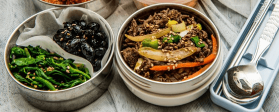 반찬통에 검정 콩자반과 녹색 시금치나물이 담겨있다. 오른쪽 반찬통엔 불고기가 가득하다.