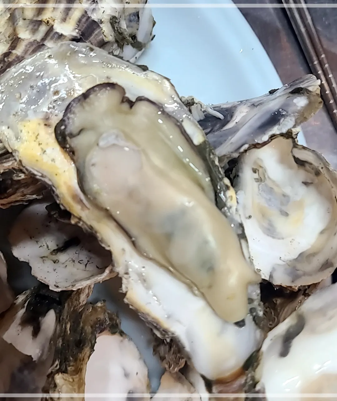 흰접시에 가득 담긴 석화찜. 석화찜 하나가 껍질이 벗겨져 있어 큰 석화알이 보임.