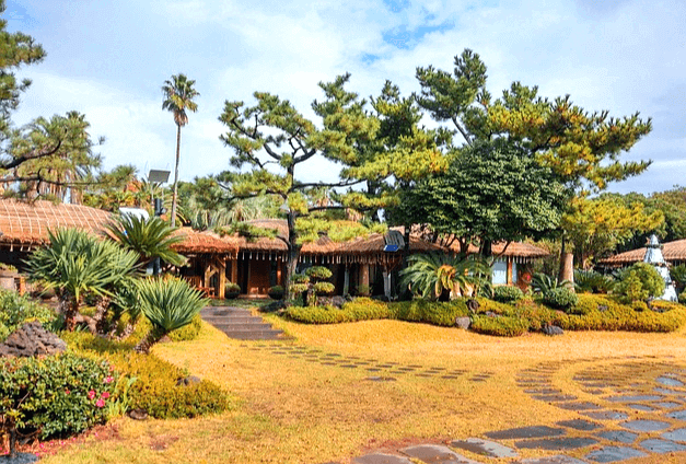 제주도 초가집들이 여러채 즐비하게 있다. 집 앞에는 푸른 잔디와 소나무들, 야자수가 가득 심어졌다.