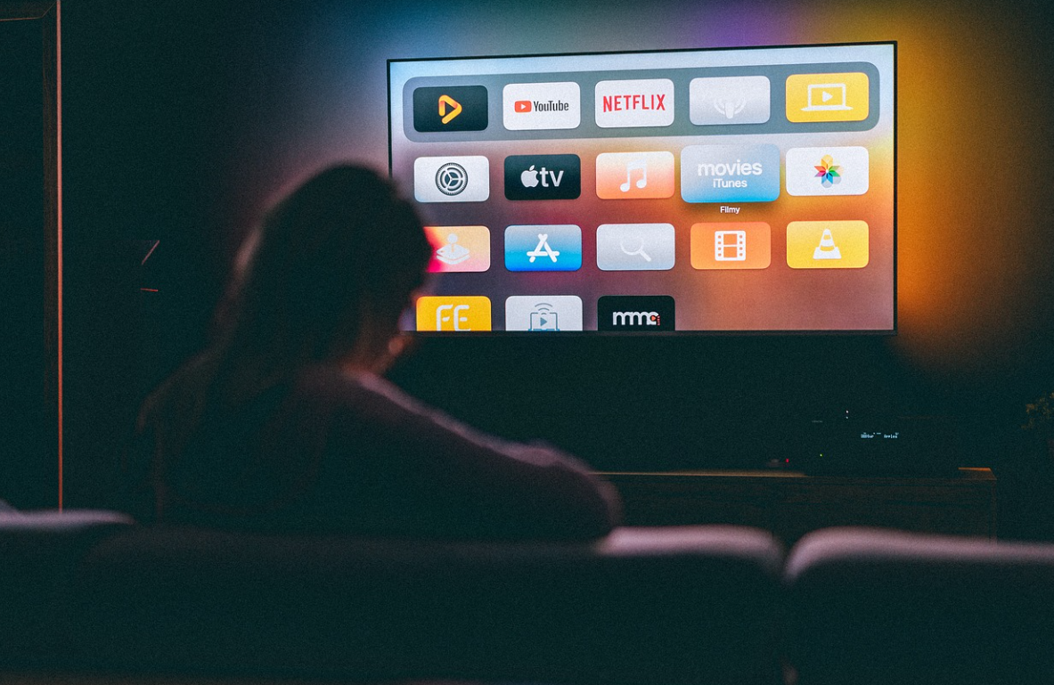 소파에 앉아 TV 화면에 있는 여러 아이콘을 보고 있는 여성의 뒷모습 사진