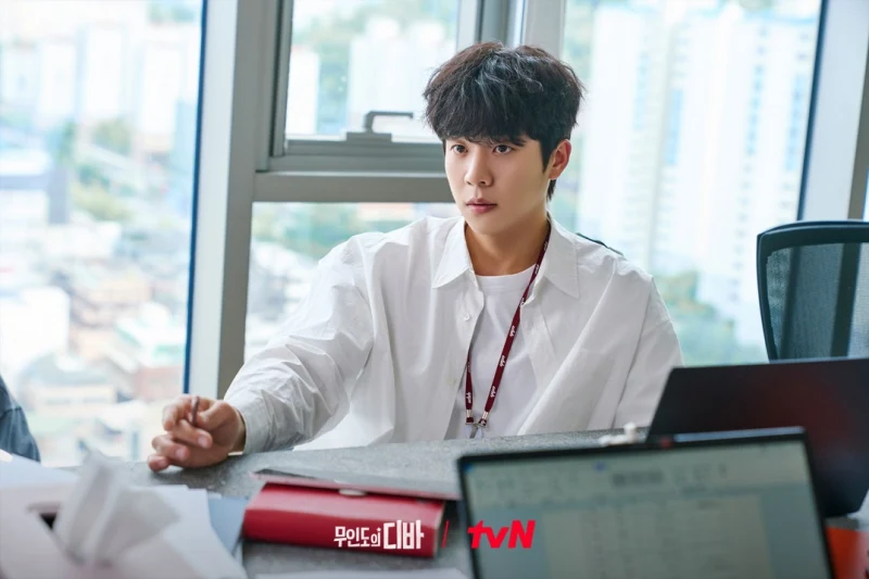 어느 사무실을 배경으로 흰 와이셔츠를 입고 앉아 있는 무인도의 디바 강보걸 캐릭터