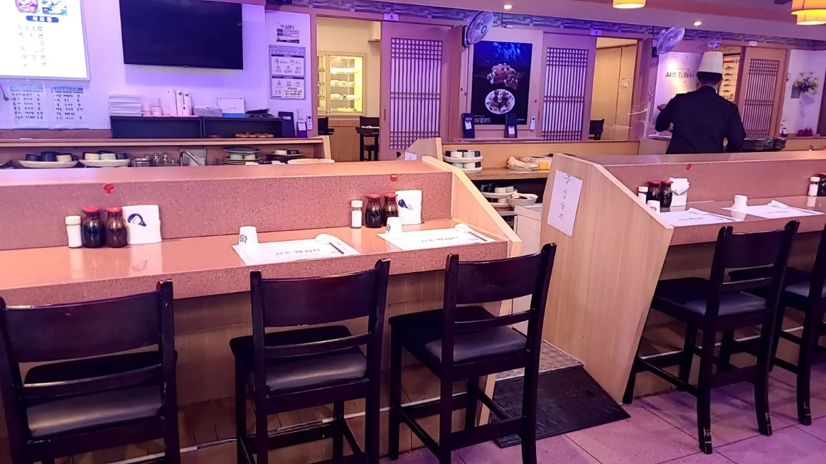 사조참치식당-나무테이블이-길게-연결된-스시바-주방장이-재료를-다듬고있다.