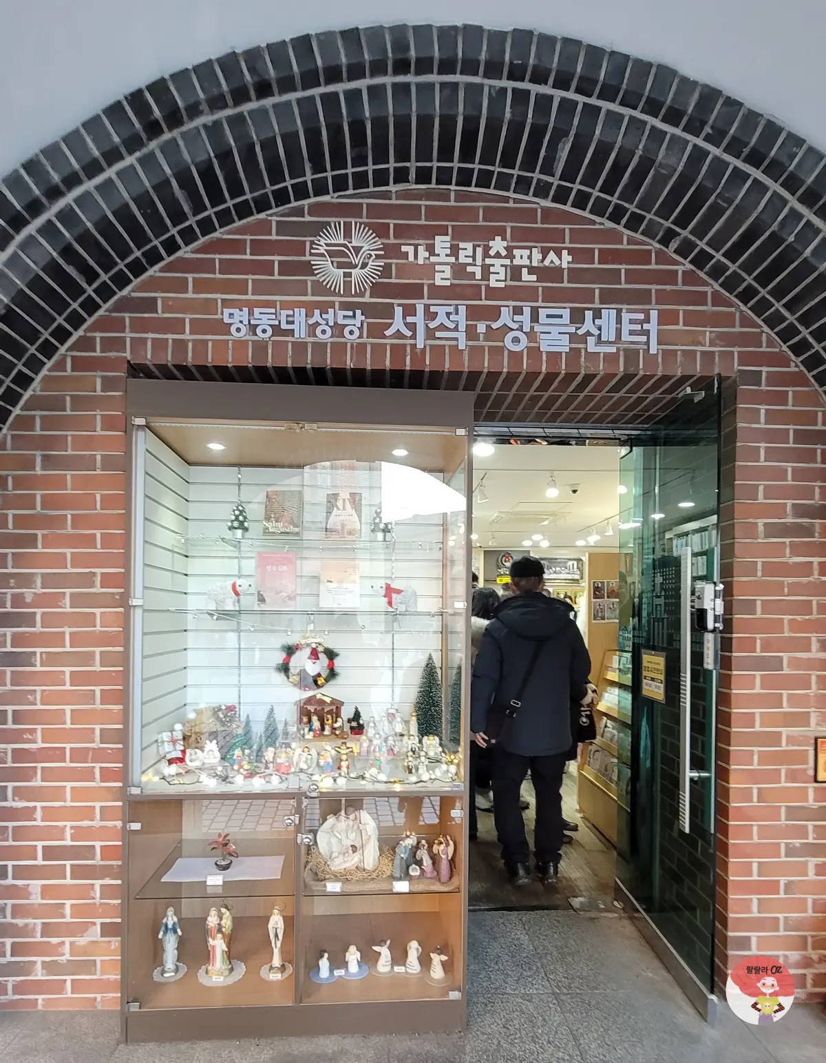 명동성당 가톨릭출판사, 진열장에는 성물들이 전시되어 있고, 내부에는 사람들이 책과 성물을 둘러보고 있다.
