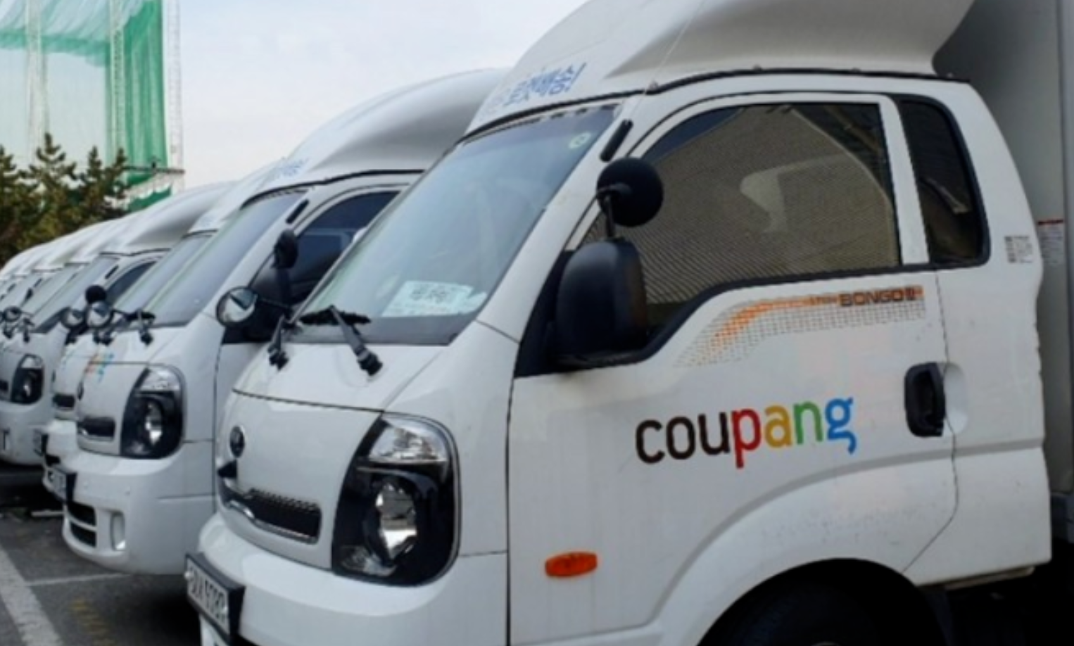 주차장에 여러대 주차되어 있는 쿠팡 배송 트럭들의 모습