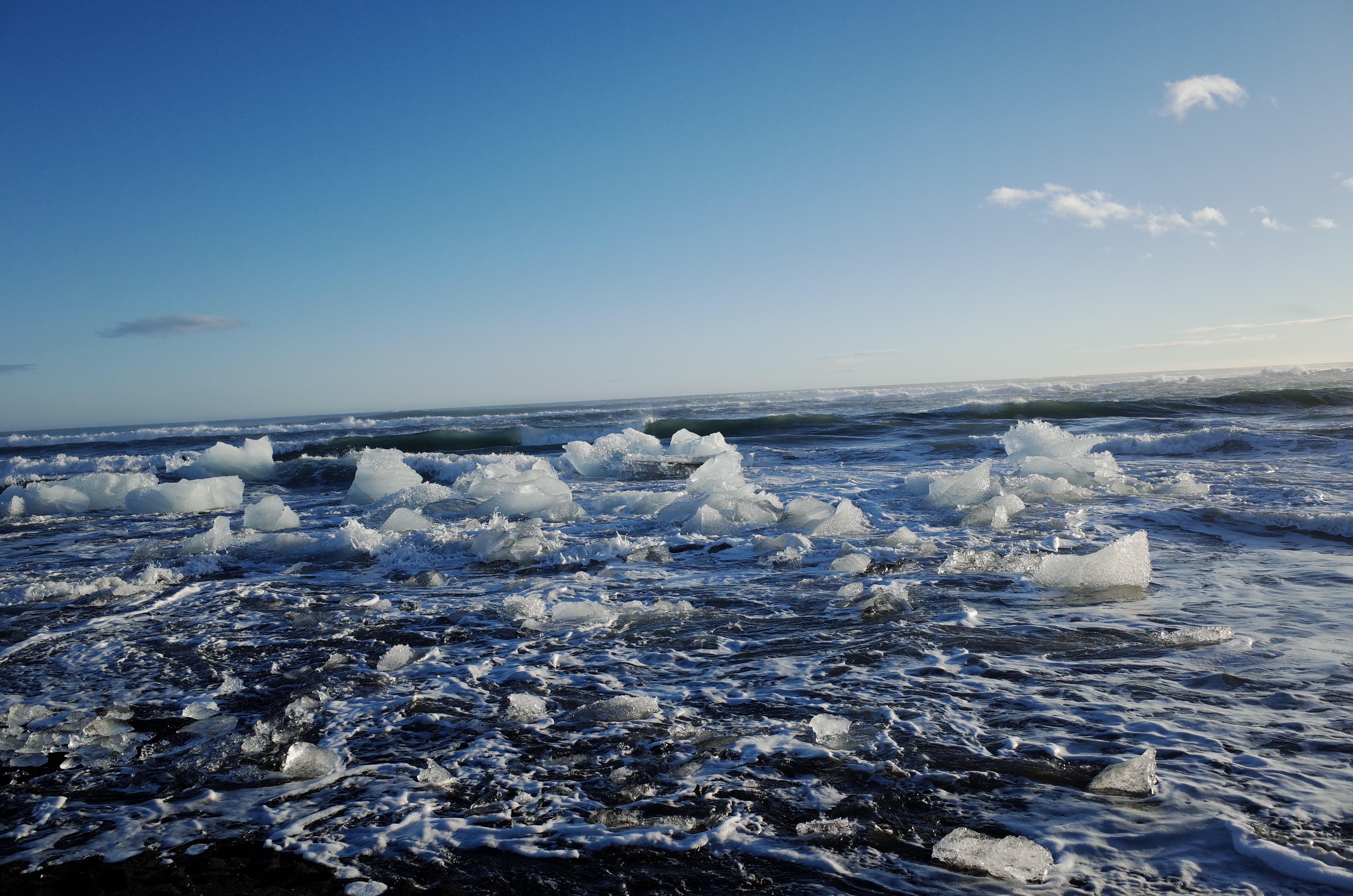 푸른 하늘 아래 파도가 치는 해안가로 밀려온 투명한 유선형 얼음 덩어리들이 장관을 이루는 다이아몬드 비치 전경