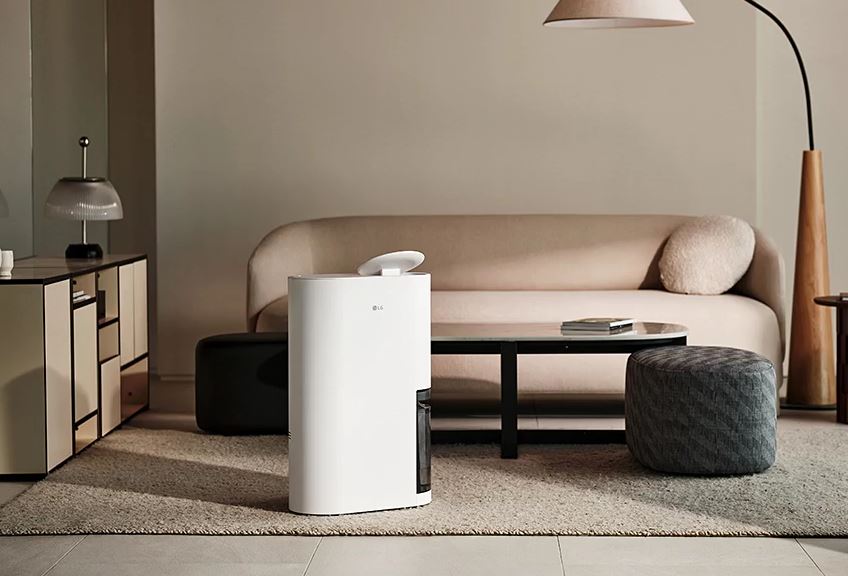 좌측에 서랍, 가운데 LG제습기 그 뒤로 위치한 탁자와 의자2개, 넓은 소파1개, 우측에 위치한 스탠딩 전등1개