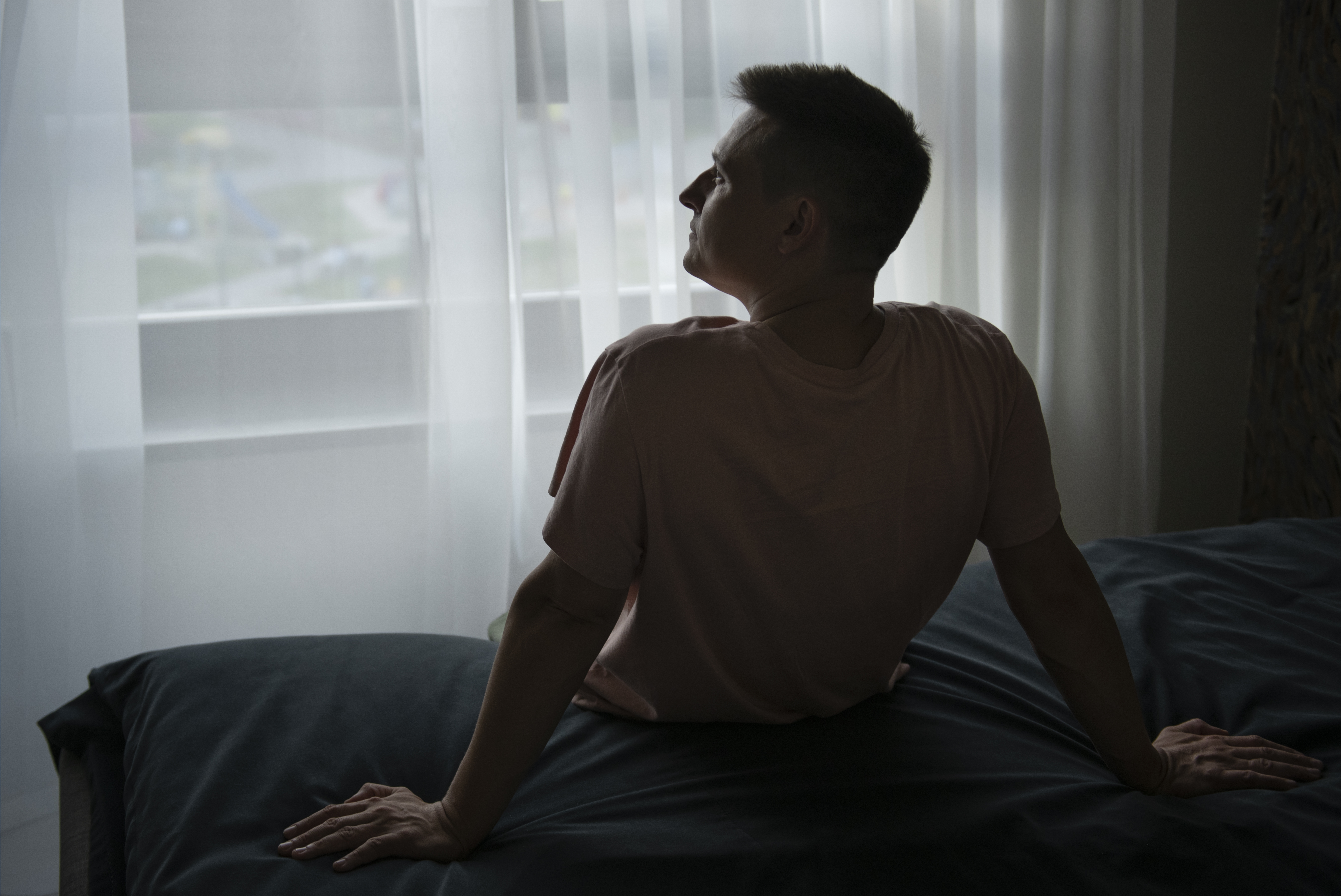 아침에 피곤함과 무기력을 느끼는 중년 남성이 침대 가장자리에 앉아 창밖을 바라보는 모습—남성 갱년기 수면장애 신호