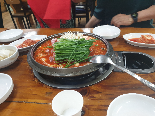 솥냄비에 전골이 들어있고 위에 버섯과 부추가 한움쿰씩 놓여있다.