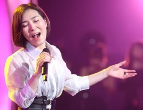 장혜진이-흰-블라우스를-입고-오른손에-마이크를-들고-열창하는-사진