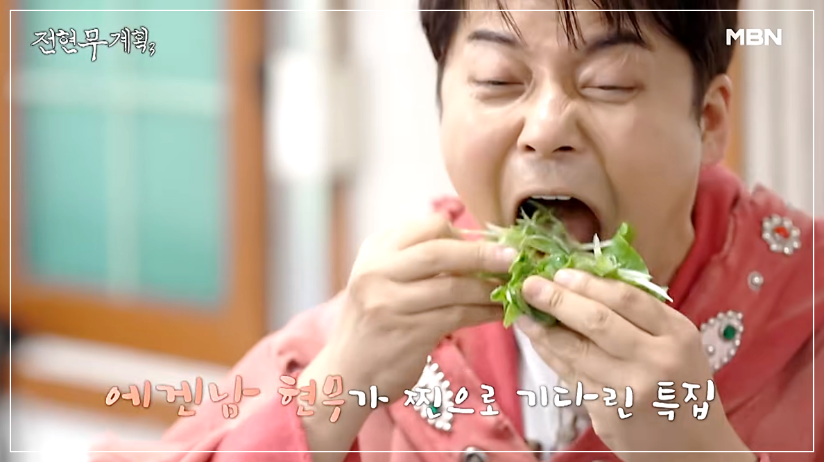 장작 난로 위에서 잘 구워진 삼겹살을 파채와 함께 쌈으로 싸서 크게 한 입 먹고 있는 전현무