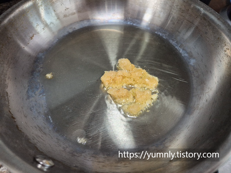 Sautéing minced garlic in a frying pan with olive oil to release fragrance.