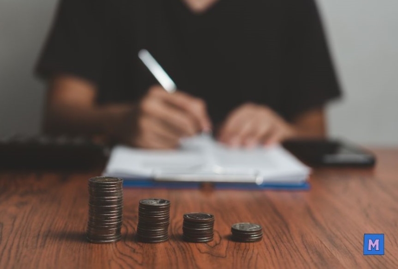 소상공인 부담경감 크레딧 계산하는 모습, 동전 스택과 계산기가 있는 책상에서 서류 작성 중 VIA CANVA