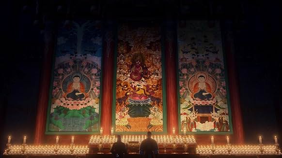 촛불 수십 개가 밝혀진 가운데 세 폭의 불교 탱화 앞에 선 두 남성의 뒷모습