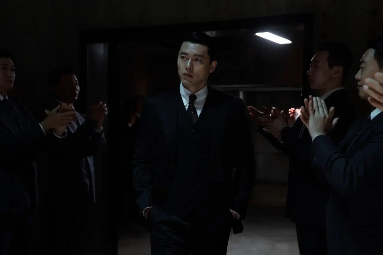 백기태가 주머니에 손을 넣고 걸어가며 그 옆으로 서있는 직원들이 모두 박수를 치고 있는 모습