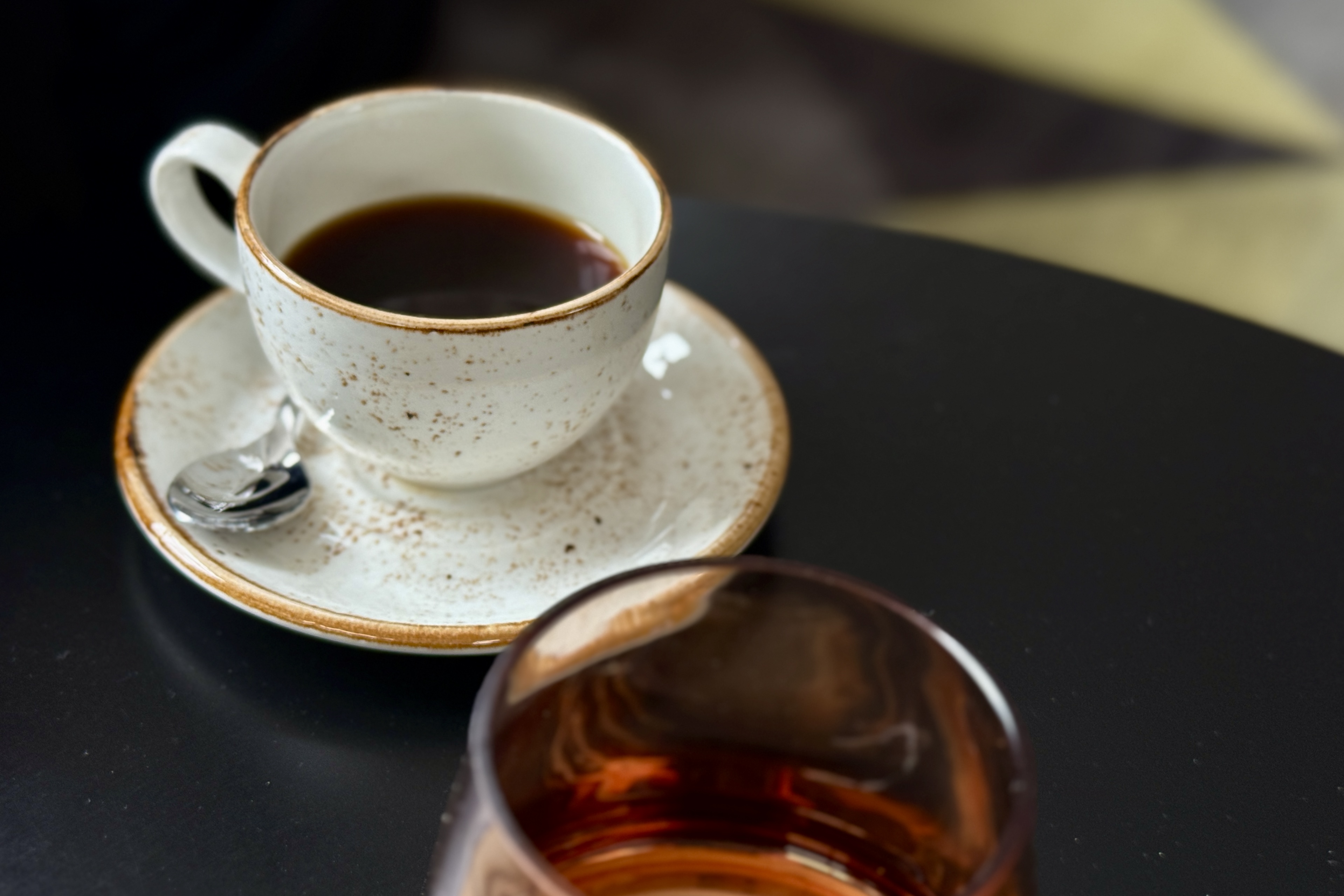 도자기 느낌의 컵에 담긴 블랙커피와 투명한 갈색 유리컵이 나란히 놓인 테이블 위 모습