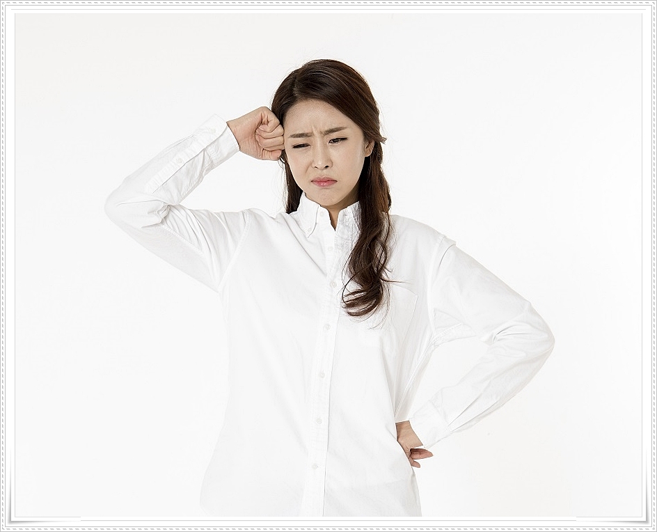 관자놀이 부근에 주먹쥔 손을 가져다 댄 채 찡그린 표정을 짓고 있는 여성의 모습