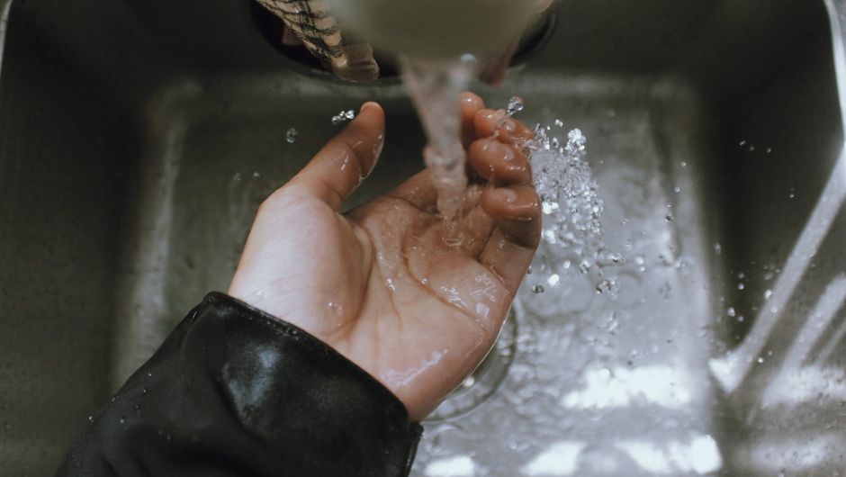 Close-up of a hand being washed under a stream of running water in a sink, emphasizing cleanliness.