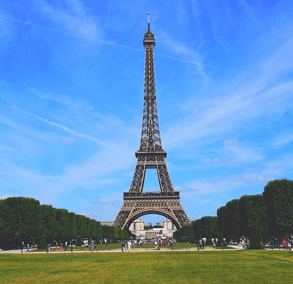 파란 하늘 아래 에펠탑이 높이 세워져 있다. 철제로 만들어진 튼튼한 탑이고 앞에는 초록색 잔디밭이 있다.