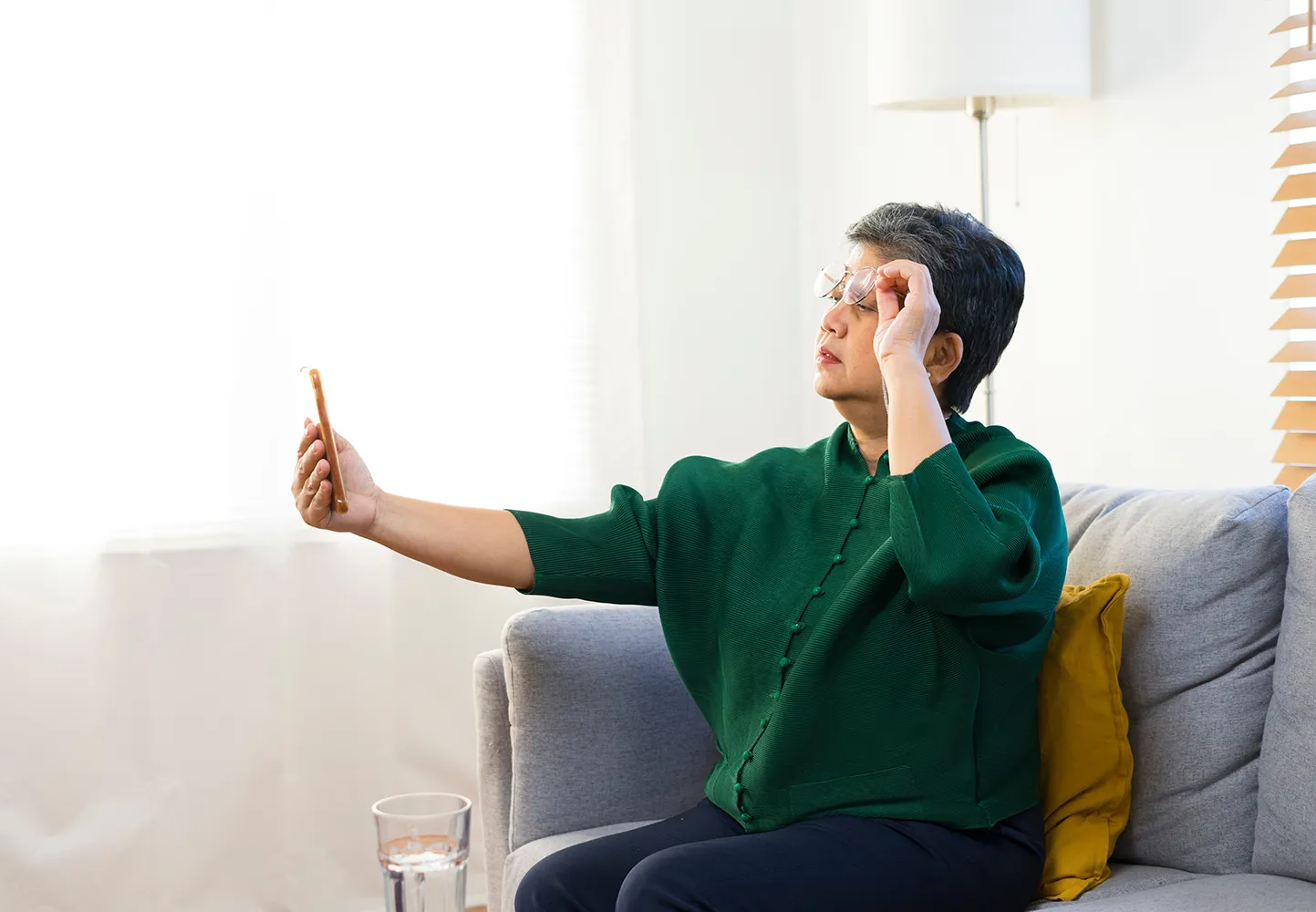 스마트폰 화면을 보며 메시지를 읽으려고 눈을 가늘게 뜨고 있는 노인 여성