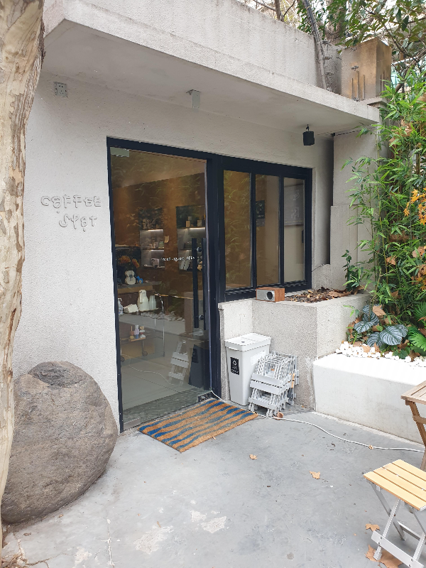 회색 외관을 가진 커피스팟. 옆에는 푸르른 나뭇잎이 계절과 다른 매력을 준다.